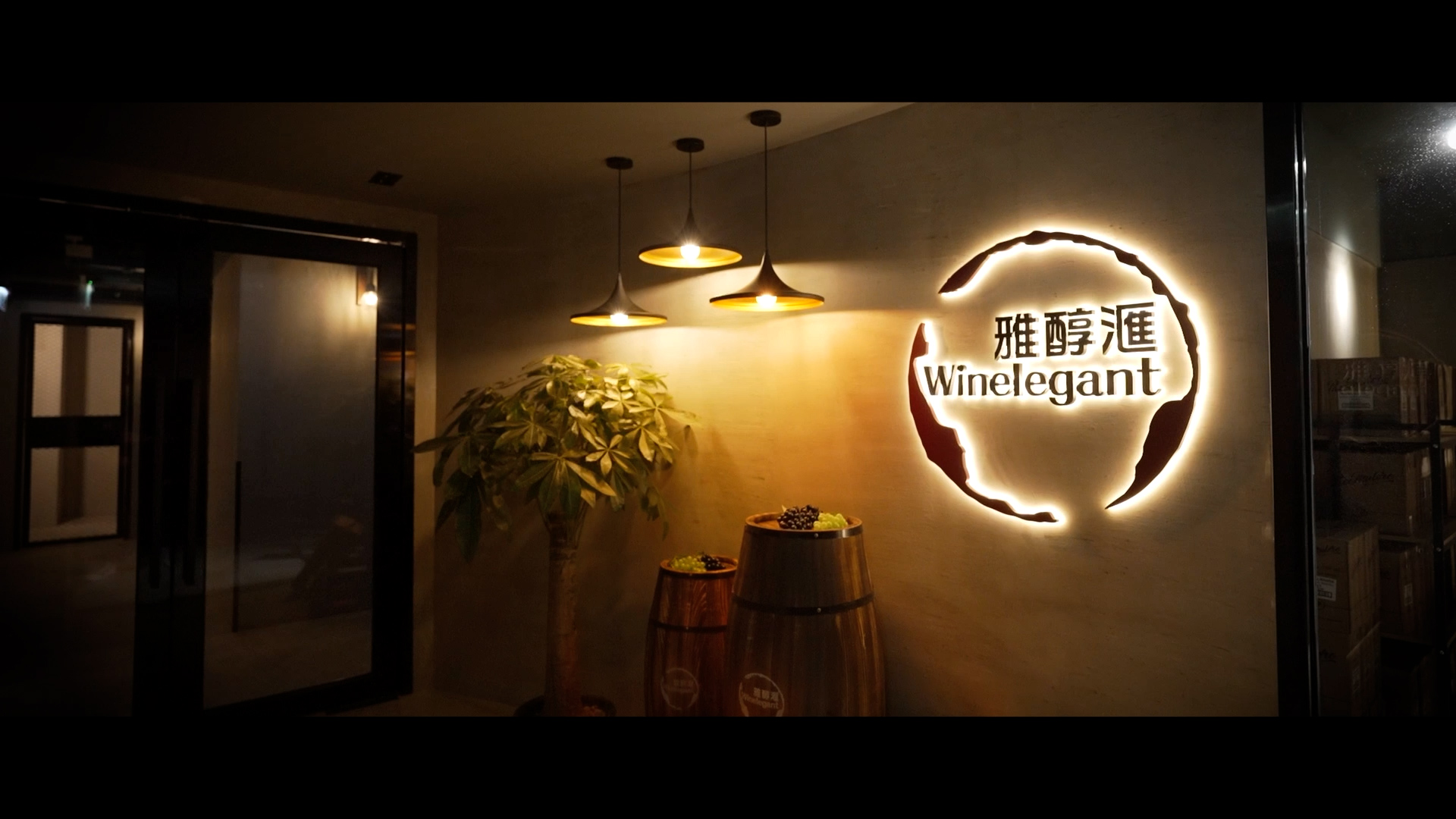 A warmly lit entrance to "Winelegant" with a glowing wall sign in English and Chinese, decorative wine barrels, a potted plant, and three hanging pendant lights.