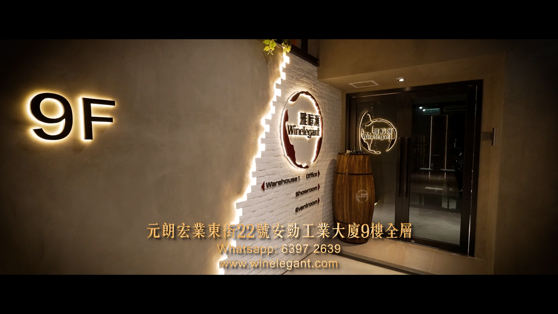 A warmly lit entrance to WineElegant with illuminated "9F" on the wall, a wooden barrel, company logo, and gold Chinese and English text providing address, WhatsApp, and website details.