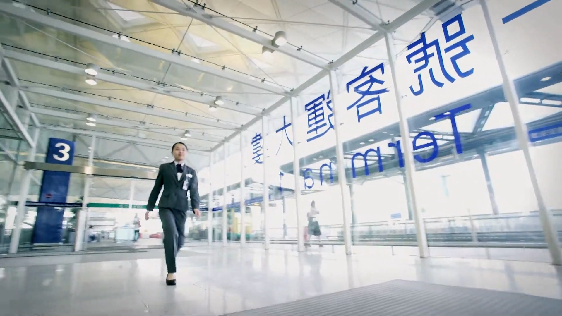 A person in a suit walks confidently through a bright, modern transit station with large glass windows and blue signage in Chinese and English.