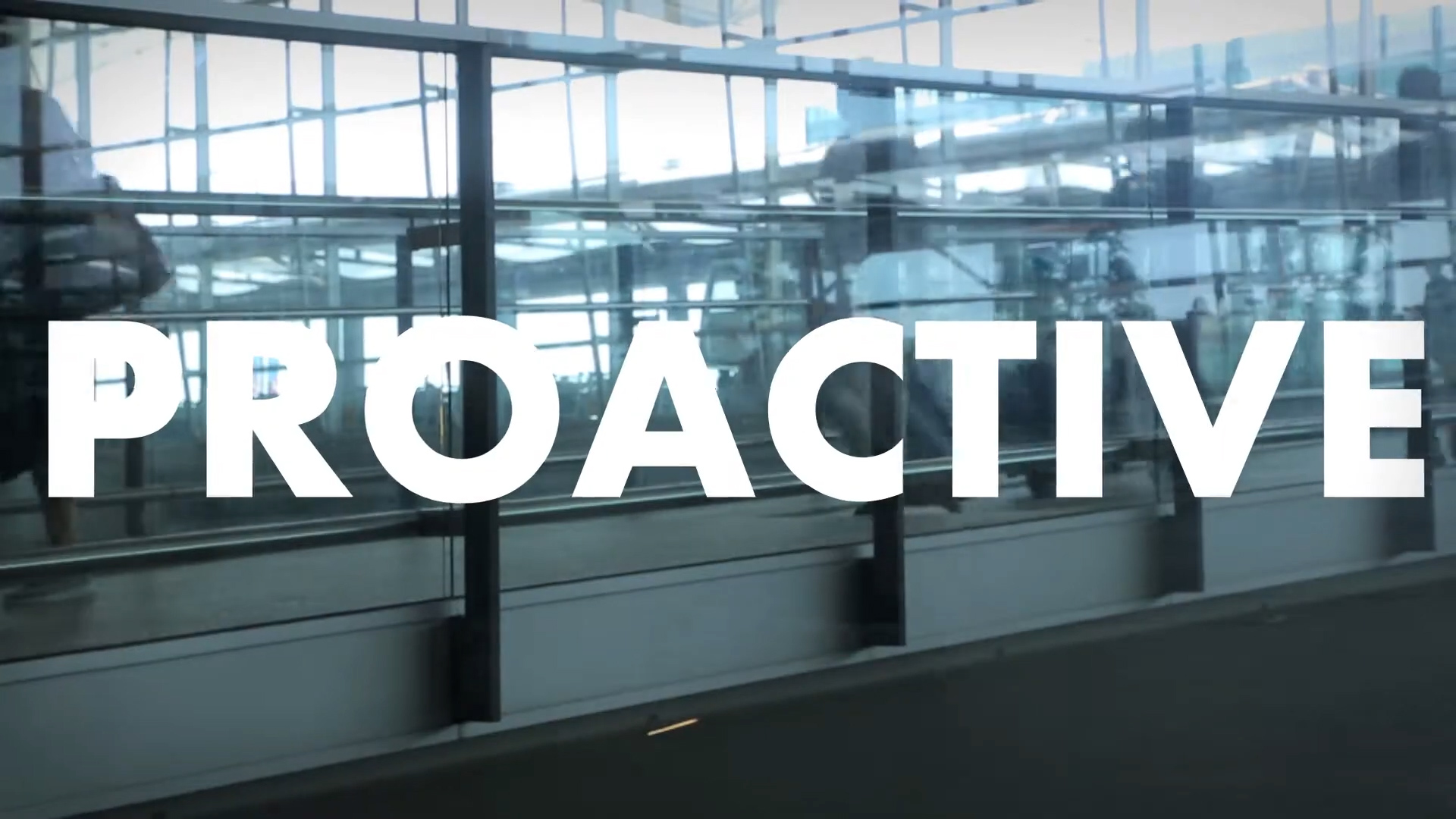 Large white text reading "PROACTIVE" is overlaid on a glass wall in a modern, sunlit building with reflections and architectural details visible in the background.